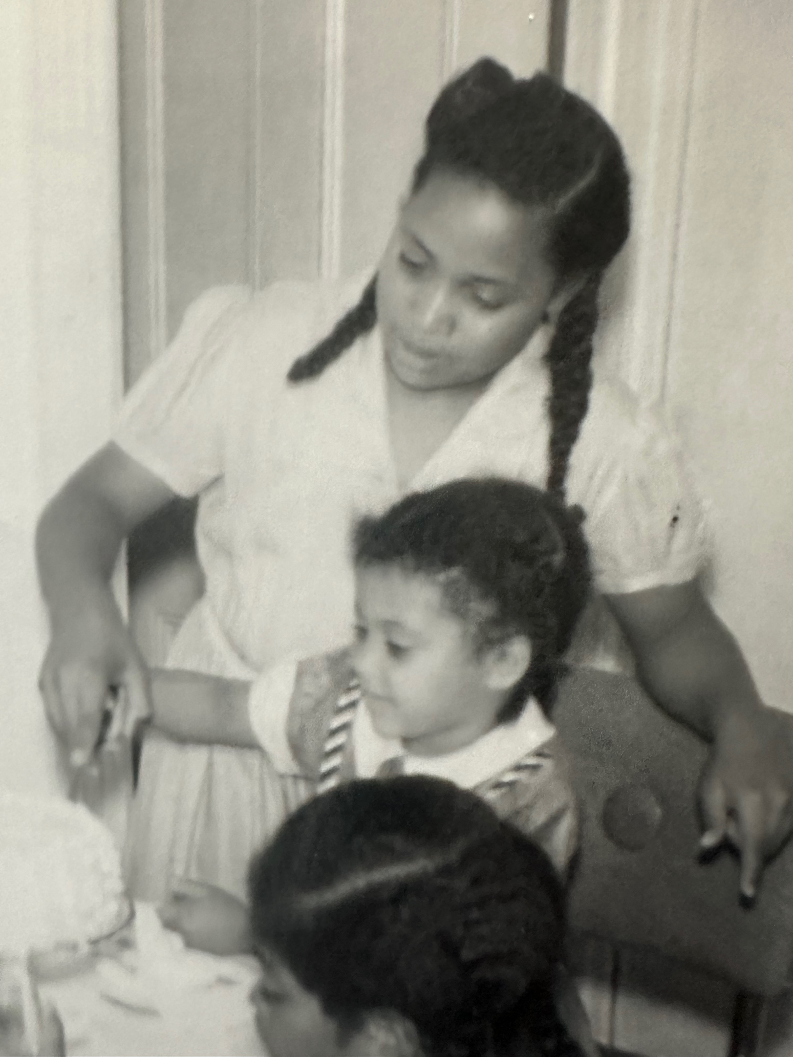 A vintage black and white photo of Karen as a young woman cutting a cake with two children